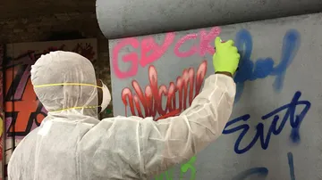 Person sprays graffiti on a wall in an urban environment.