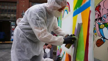 Two people spray paint on an outdoor wall.