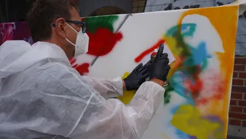 A man is spraying paint onto an outdoor canvas.