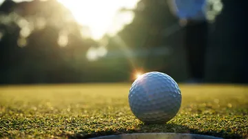 Golfball liegt auf dem Grün, während jemand spielt.