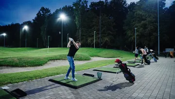 Golfer hits the ball on an illuminated driving range.