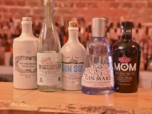 There are five gin bottles on a wooden counter.