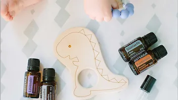 Holz-Dinosaurier mit Babyfuß und ätherischen Ölen daneben.