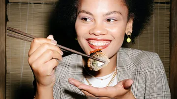 Woman holding sushi with chopsticks in a restaurant.