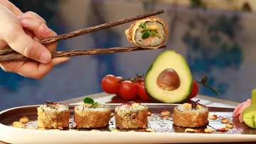 Frittierte Sushi wird mit Essstäbchen angehoben, umgeben von Gemüse.