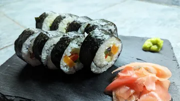 Sushi rolls lie on black stone with ginger and wasabi.