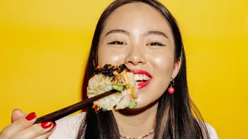 Frau genießt Sushi mit Essstäbchen vor gelbem Hintergrund.