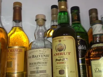 Flaschen mit Whisky stehen auf einem Regal hintereinander.
