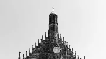 Turm mit Uhr, erhebt sich über städtischem Hintergrund in Schwarz-Weiß.