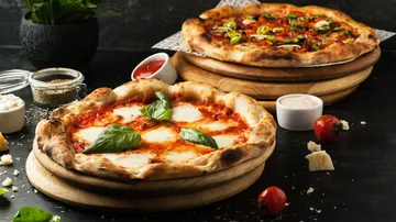 Two pizzas lie on wooden plates, one with fresh ingredients.