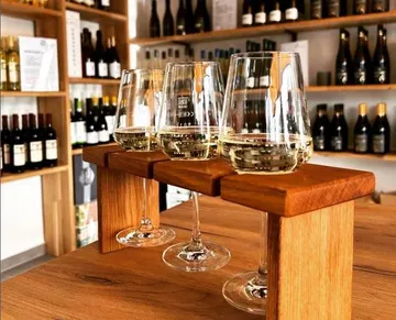 Three wine glasses stand on a wooden rack in a wine shop.