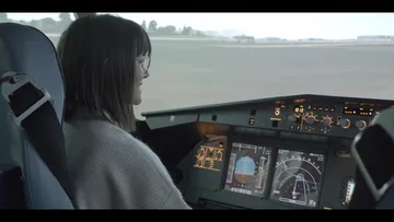 Frau sitzt im Cockpit und steuert den Simulator.