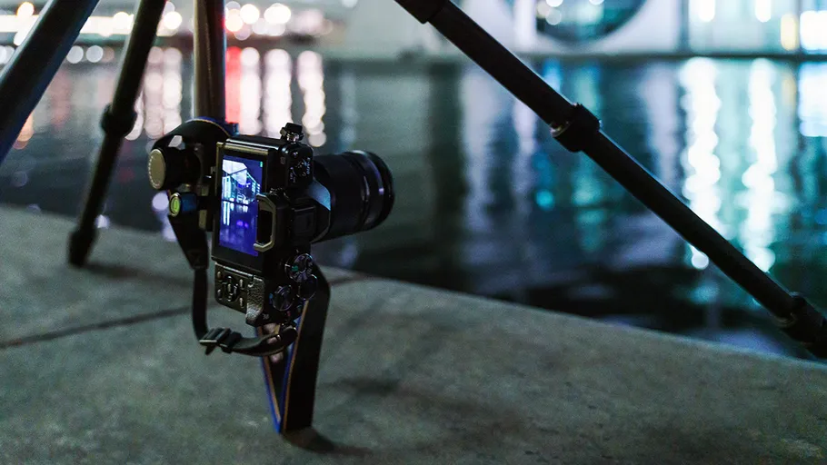 Camera stands on a stand, photographs calm water at night.