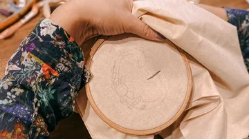 Hand holding an embroidery frame with an unembroidered motif.