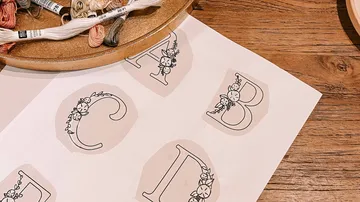 Karten mit Buchstaben, umgeben von Stickgarn auf Holzoberfläche.