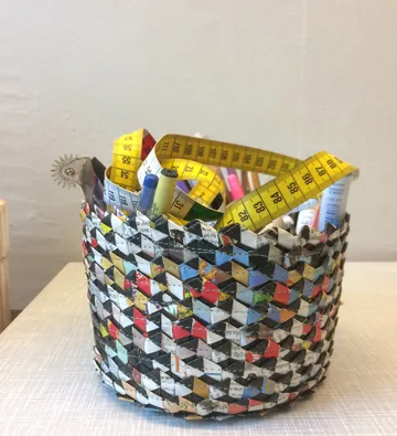 Geflochtener Korb mit Stiften und Maßband, auf Tisch.