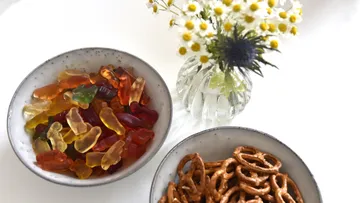 Colourful gummy bears and pretzels in bowls, flowers next to them.