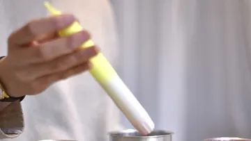 Yellow syringe holds over a container in a bright environment.