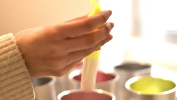 One hand holds a piping bag over cups.