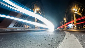 Lichter von Fahrzeugen bewegen sich über eine Brücke nachts.