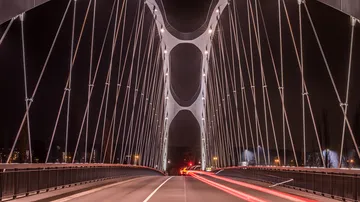 Moderne Brücke leuchtet nachts, Autos fahren darüber.
