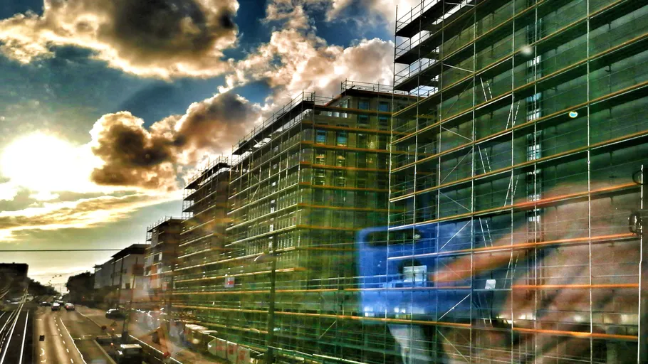 Scaffolding surrounds modern buildings under cloudy skies.