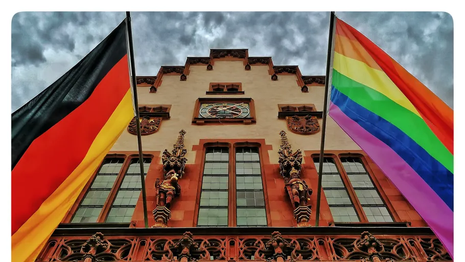 Two flags fly in front of a historic façade.