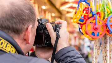 Photographer holds camera and photographs colored toys in the market.