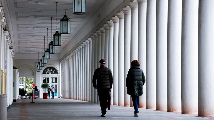 Two people walking under a row of columns.