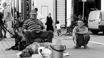 Zwei Männer sitzen auf der Straße, Hund ruht sich in der Nähe aus.