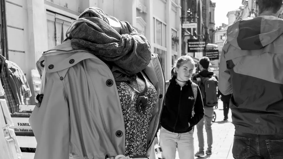 Mannequin wears layered clothes on busy street.