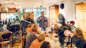 A man explains wine before a round table in a shop.