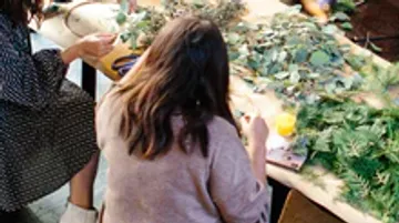 Personen basteln mit Pflanzenmaterial auf einem Tisch.