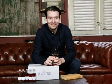 Mann hält ein Glas, sitzt auf Couch mit Flaschen.