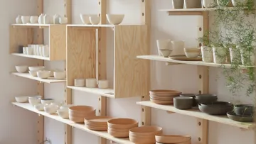 Shelves with ceramic tableware are presented in a bright environment.