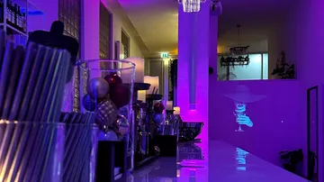 Glass with drink, projected figure, purple illuminated bar.