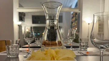 Glasbehälter mit Wasser, daneben Kartoffelchips auf Tisch.