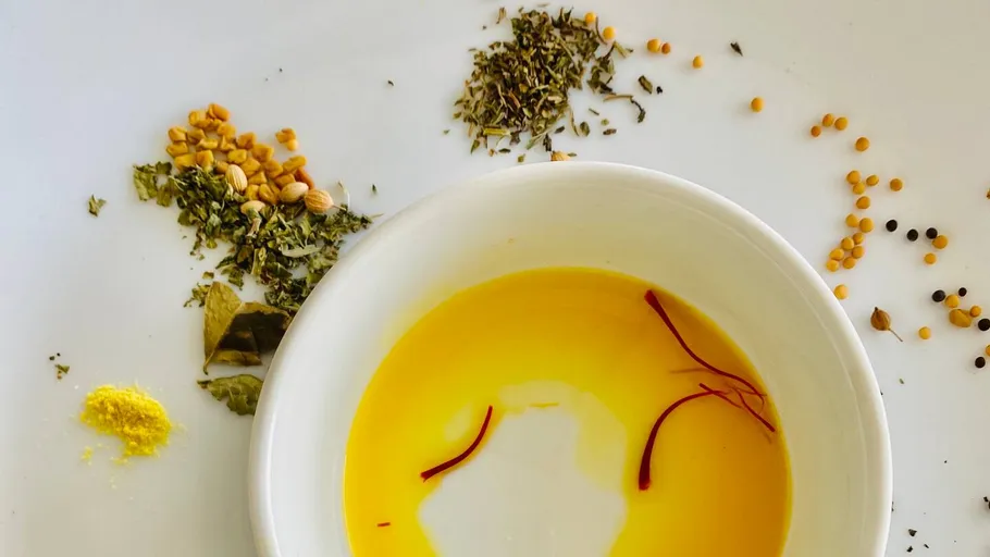 Bowl with yellow oil and various spices on plate.