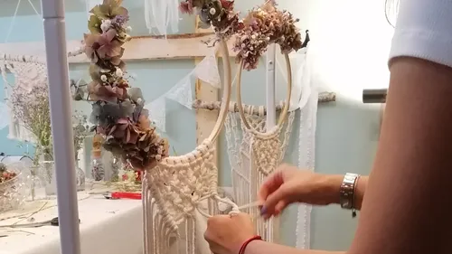 Woman knotting macrame with decorative flowers in the background.