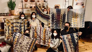 Human groups present handmade, colorful cloths in a studio.