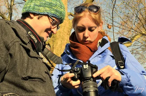 Two people are checking a camera outdoors in sunlight.