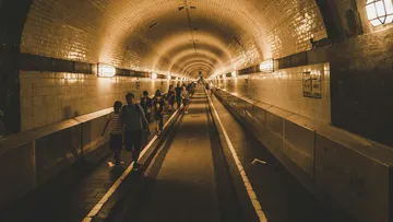People walk through an illuminated tunnel with tiles.