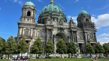 Berliner Dom mit Kuppeln, unter blauem Himmel und Bäumen.