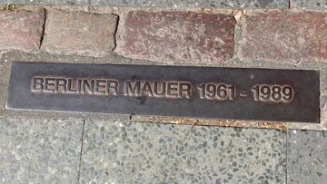 Metallplakette erinnert an Berliner Mauer zwischen Pflastersteinen.