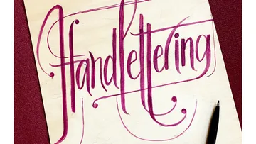 Hand lettering on wooden plate, with pen next to it.