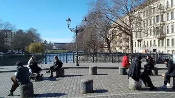 People sit on stones surrounded by trees and water.