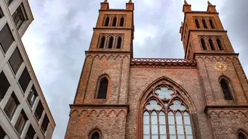 Two towers of an old church above modern buildings.