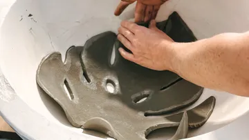 Hände formen Betonteile in einer runden Schüssel.