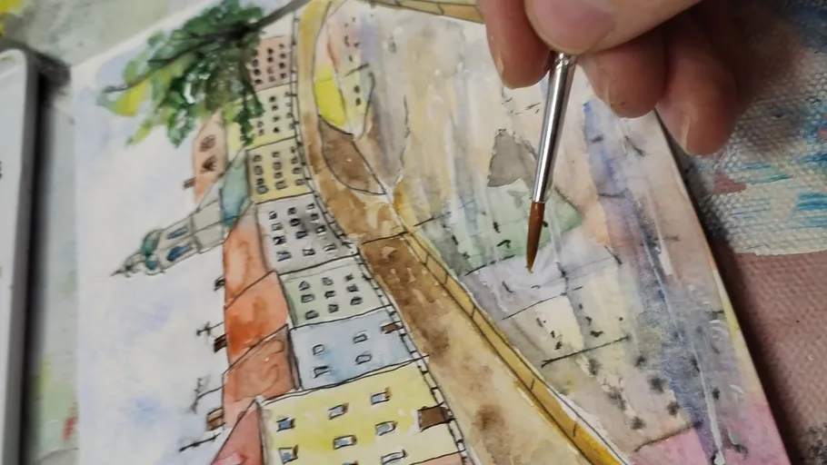 A hand paints with a brush on a watercolor drawing.