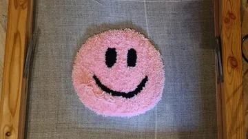 Lächelndes, pinkes Kissen liegt auf grauem Stoff.